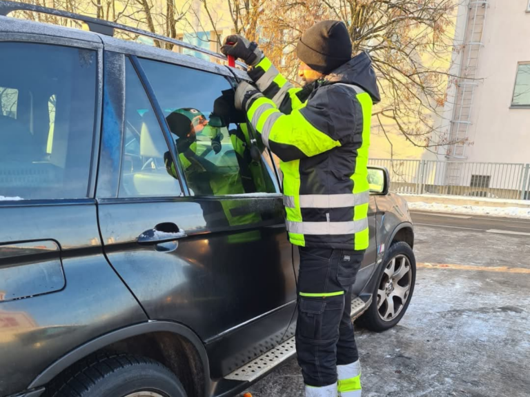 Technik w zimowej odzieży otwierający awaryjnie SUV-a marki BMW na oblodzonym chodniku.