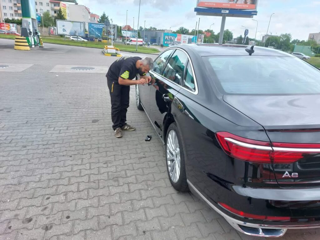 Technik przeprowadzający awaryjne otwieranie samochodu Audi A8 przy stacji benzynowej.