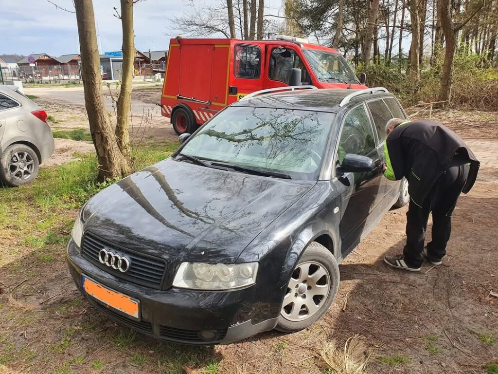 Awaryjne otwieranie drzwi starszego modelu Audi zaparkowanego w pobliżu lasu.