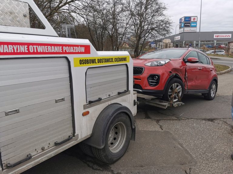 Laweta transportująca czerwony samochód osobowy uszkodzony w kolizji drogowej.