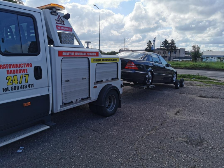Laweta transportująca czarny samochód osobowy na poboczu drogi w słoneczny dzień.