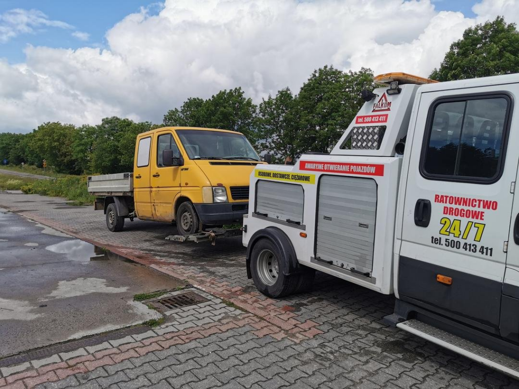 Laweta przewożąca żółtego dostawczaka na poboczu drogi przy leśnej alei.