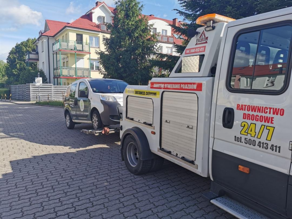 Laweta transportująca duże auto na tle miejskiego osiedla.
