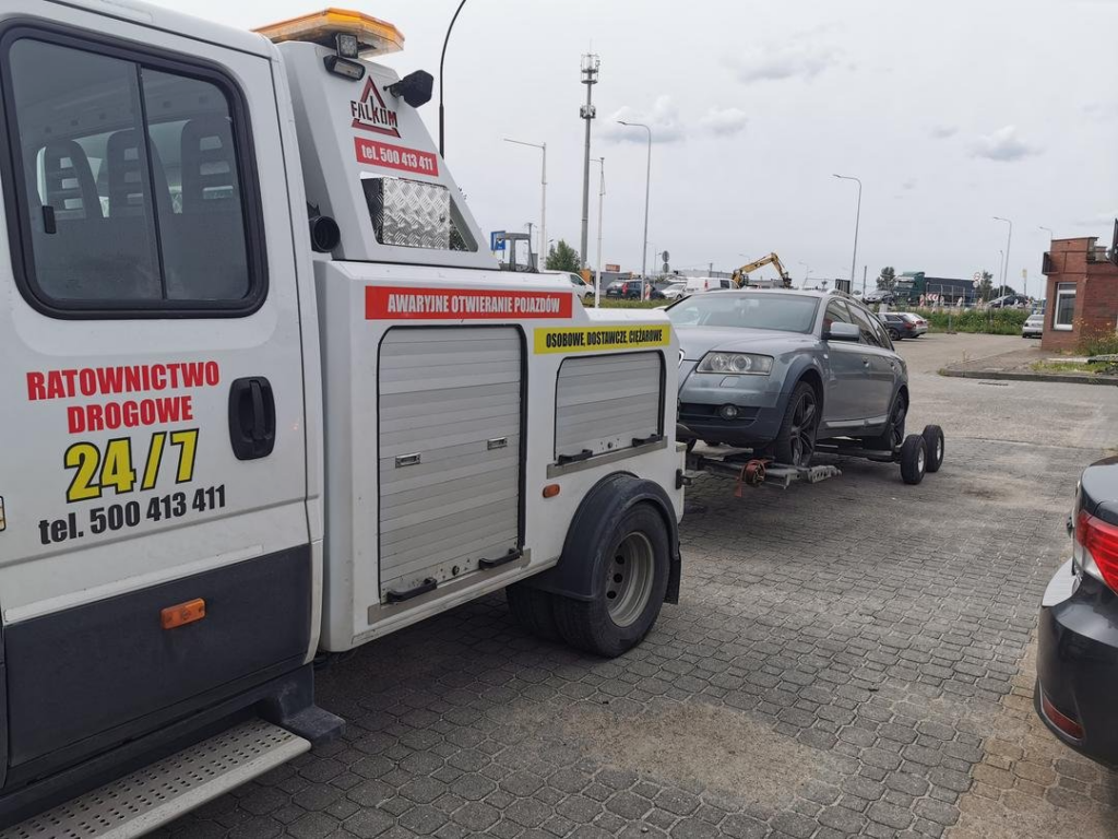 Holowanie srebrnego auta osobowego na placu przed serwisem wulkanizacyjnym.