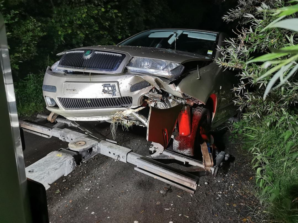 Uszkodzona Skoda z poważnym zderzeniem czołowym holowana nocą z leśnej drogi.