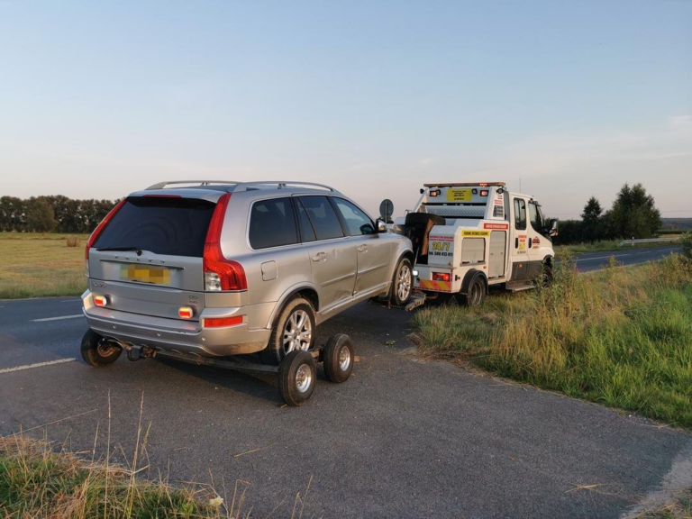 Laweta transportująca szary samochód osobowy na poboczu drogi.