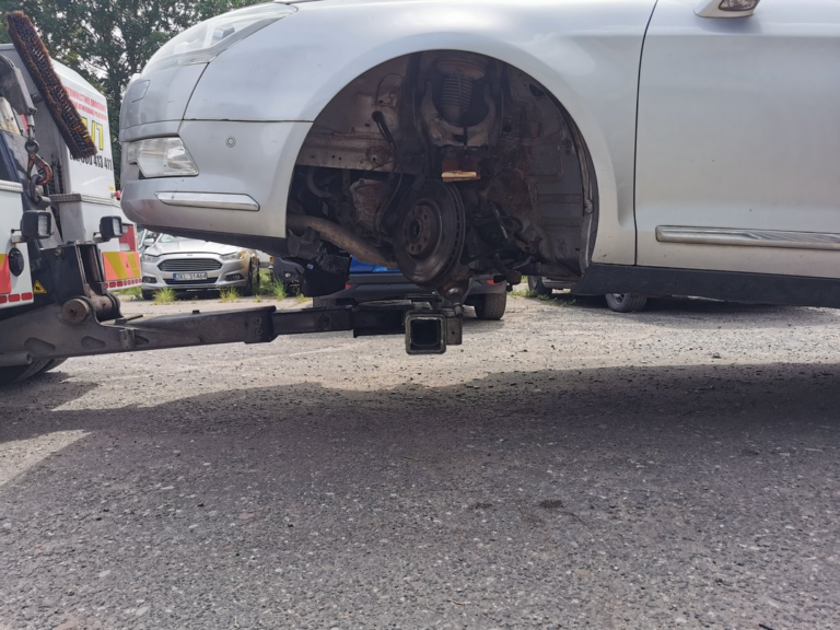 Zbliżenie na uniesiony przód samochodu bez koła, przygotowanego do transportu lawetą.