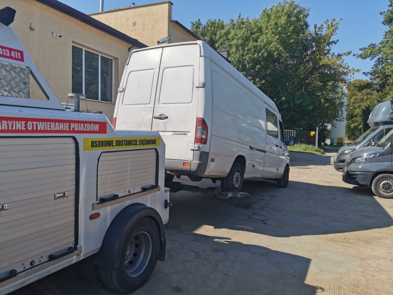Laweta holująca biały samochód dostawczy na terenie zakładu.