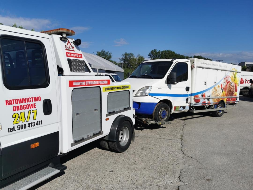 Uszkodzony czarny ciągnik siodłowy z naczepą w trakcie akcji ratowniczej poza miastem.