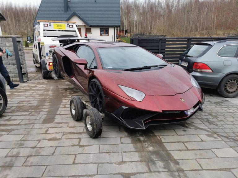 Luksusowy samochód sportowy Lamborghini holowany przez lawetę przed domem jednorodzinnym.