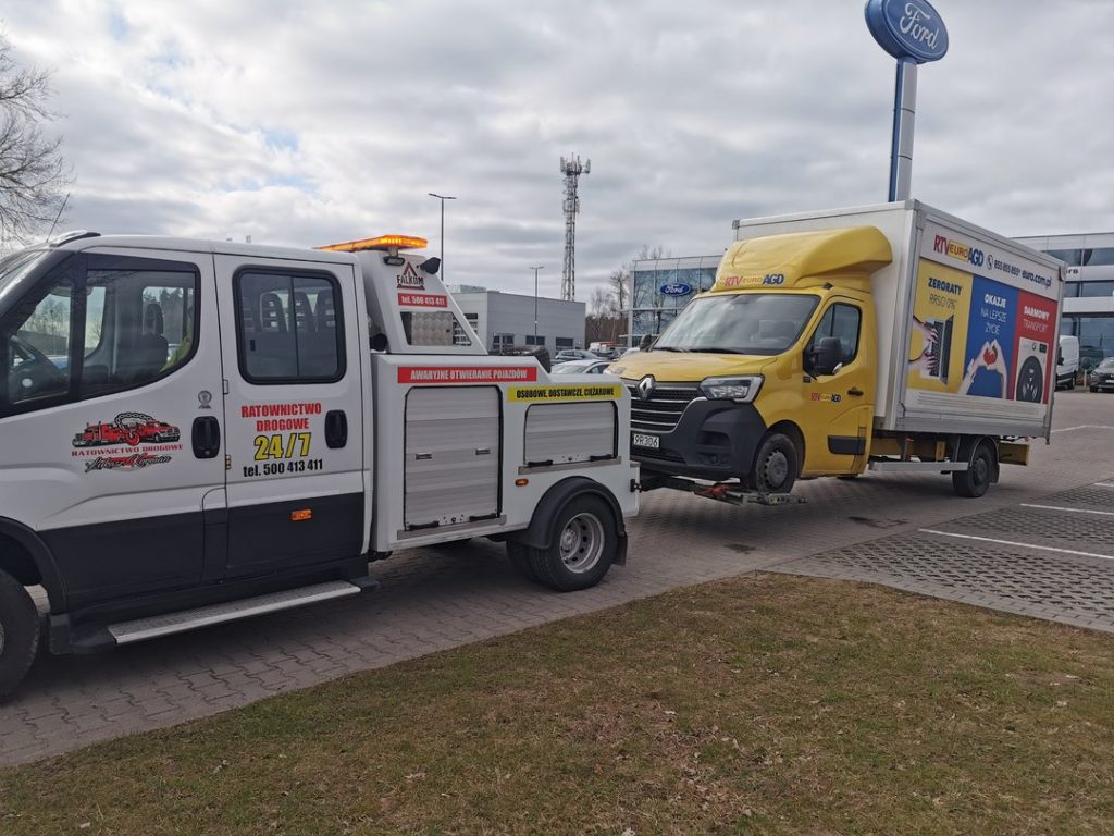Pomoc drogowa przewożąca żółty samochód dostawczy.