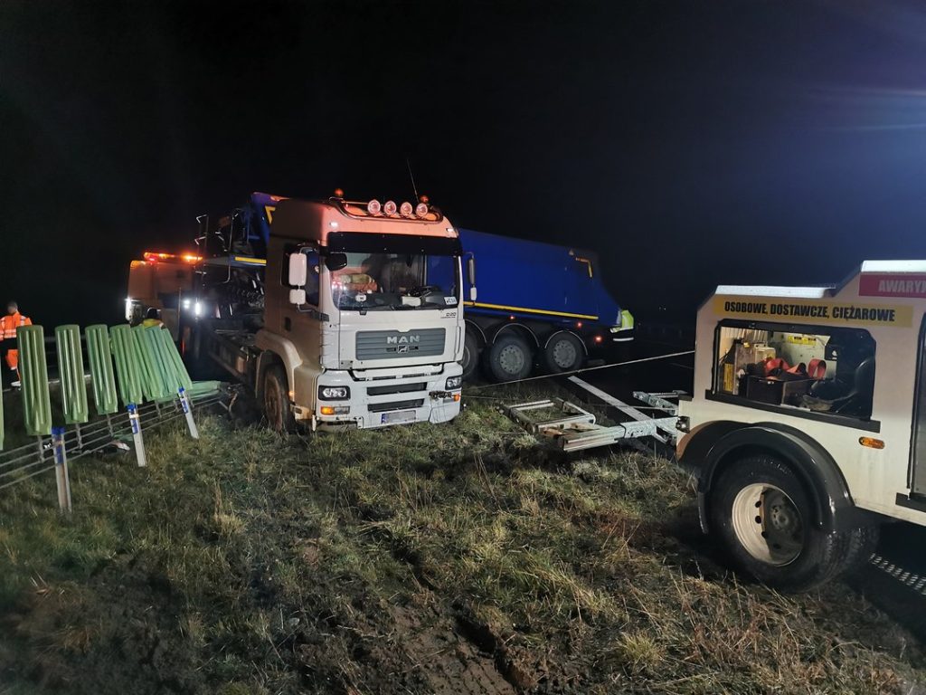 Akcja ratownicza ciężarówki na poboczu drogi w nocy z udziałem pojazdu specjalistycznego.