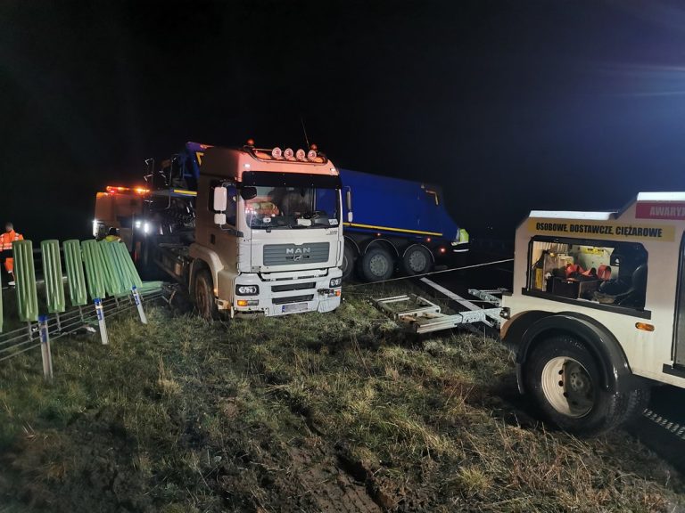 Akcja ratownicza ciężarówki na poboczu drogi w nocy z udziałem pojazdu specjalistycznego.