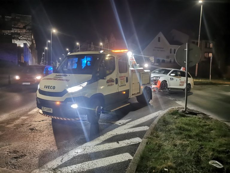 Laweta holująca uszkodzony samochód osobowy w nocy.