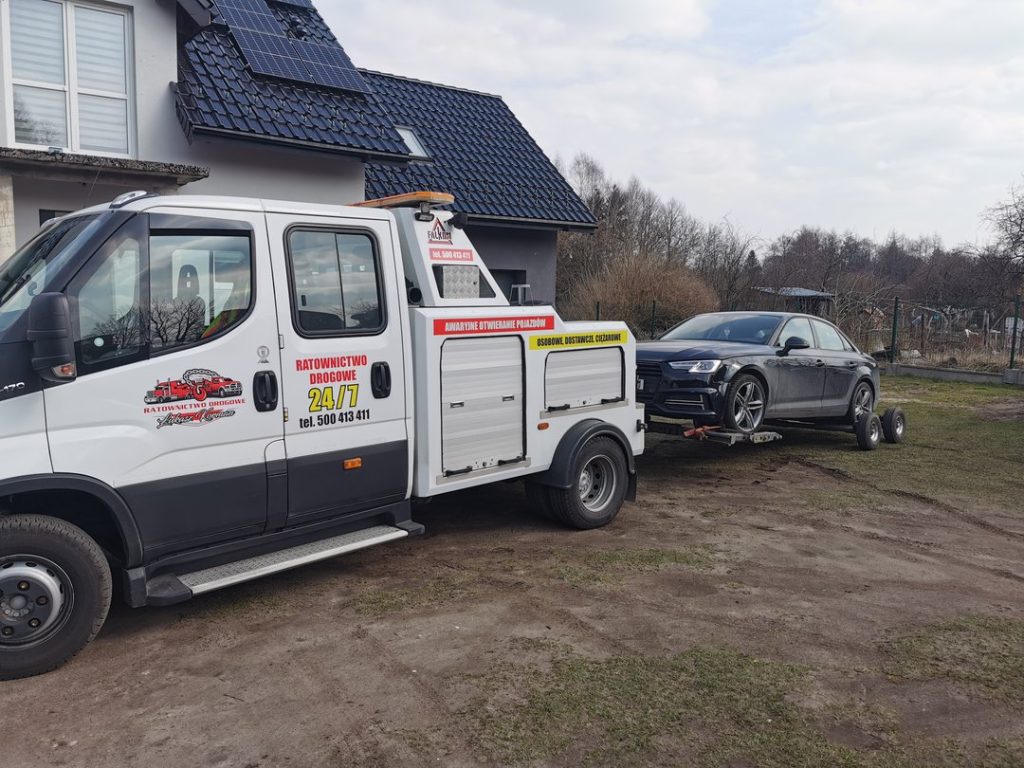 Laweta przewożąca czarny samochód osobowy przed domem jednorodzinnym.