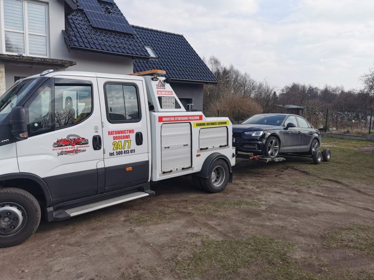 Laweta przewożąca czarny samochód osobowy przed domem jednorodzinnym.