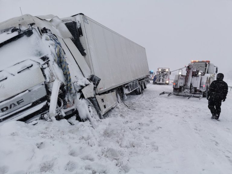 Ciężarówka w rowie podczas śnieżycy, w trakcie akcji ratowniczej z udziałem specjalistycznych pojazdów.
